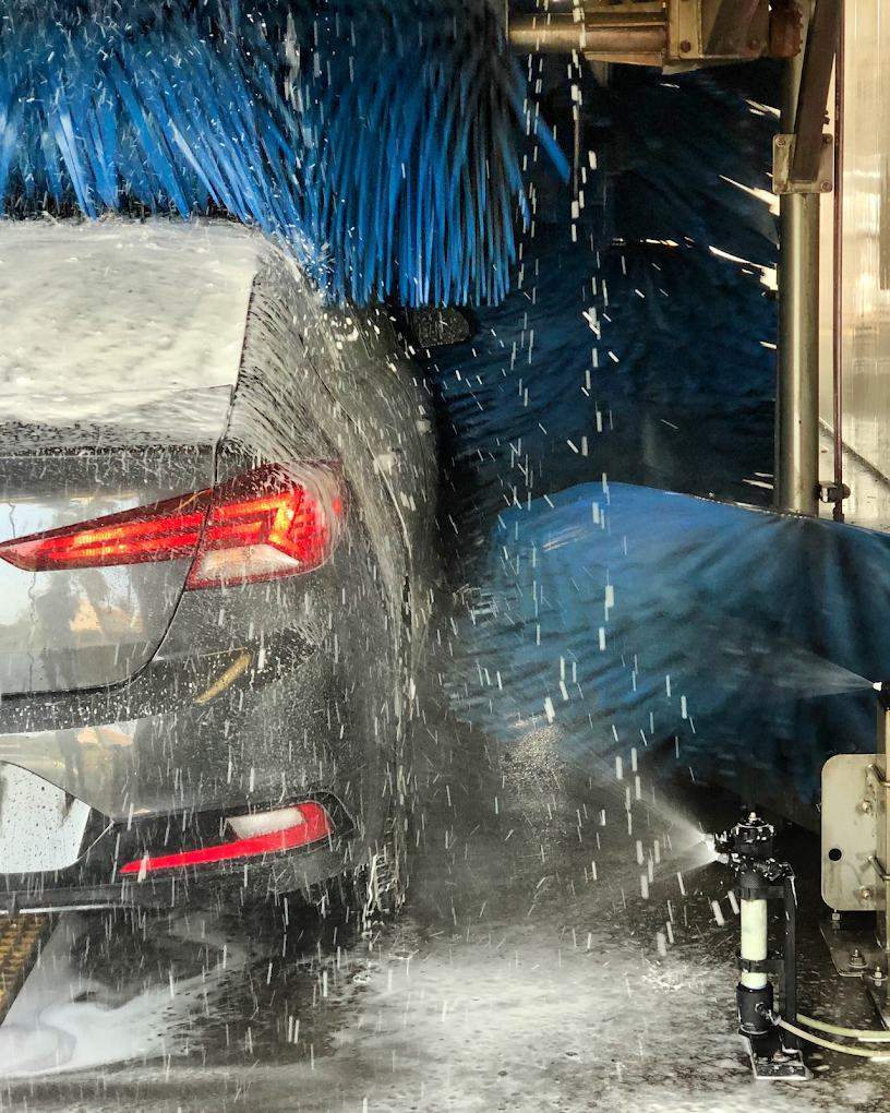 Gray sedan inside the Jurupa Valley tunnel with blue soft-touch brushes and water spraying across the paint