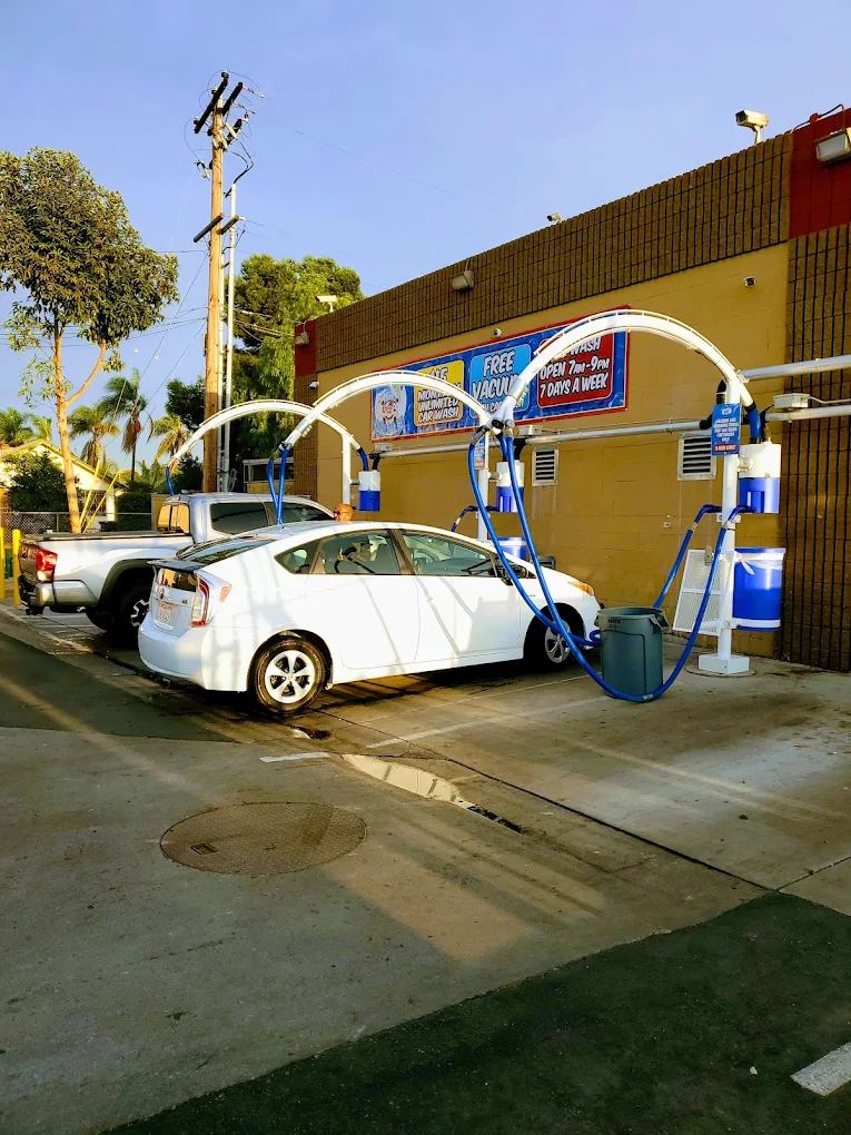 White car parked under the blue free-vacuum arches at the San Diego location, with the Free Vacuums and Open 7am to 9pm signs on the building